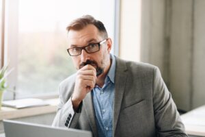 A man in glasses looks skeptically at the camera.