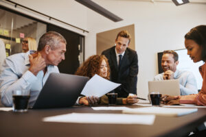 A group of people sitting at a table working and looking at papers.