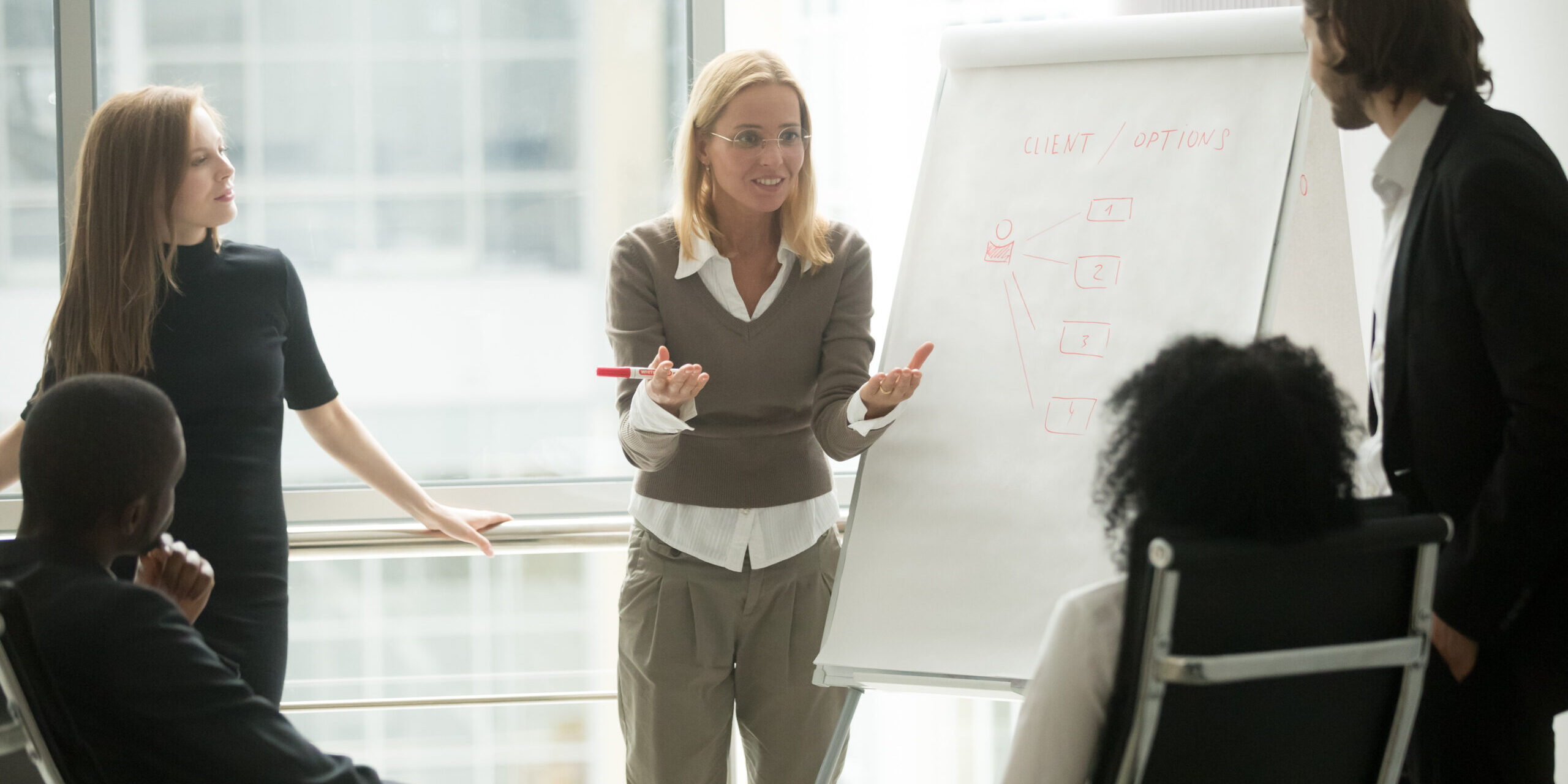 A woman gives a presentation in front of an easel to a group of people.