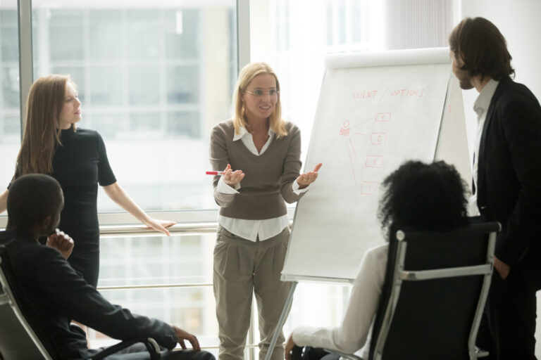 A woman gives a presentation in front of an easel to a group of people.