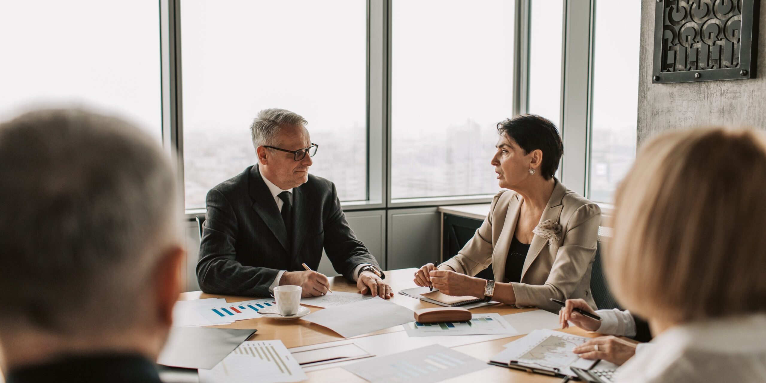 Four people have a discussion around a table, scattered with papers.