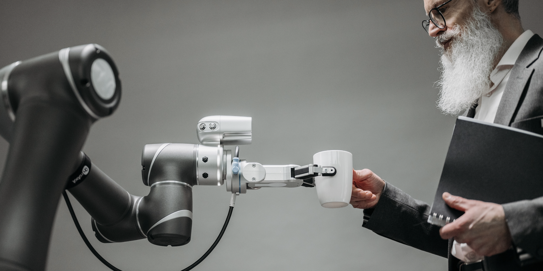 A man takes a mug from a machine, which holds the mug out towards him with a robotic limb.