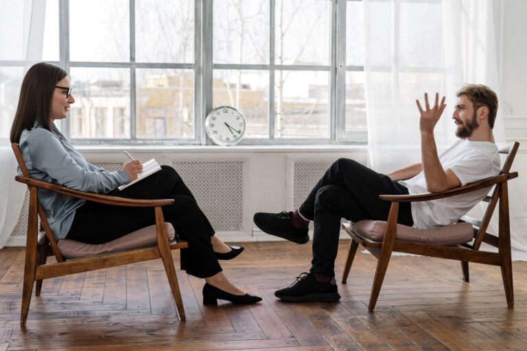 A woman counseling a man in a bright room.