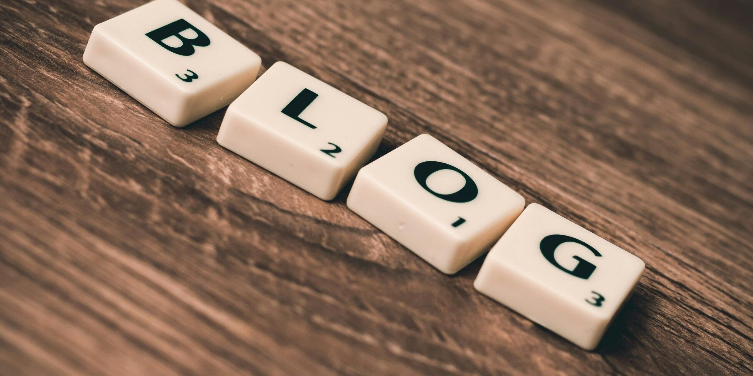 Scrabble tiles arranged to spell "blog" on a wooden surface.