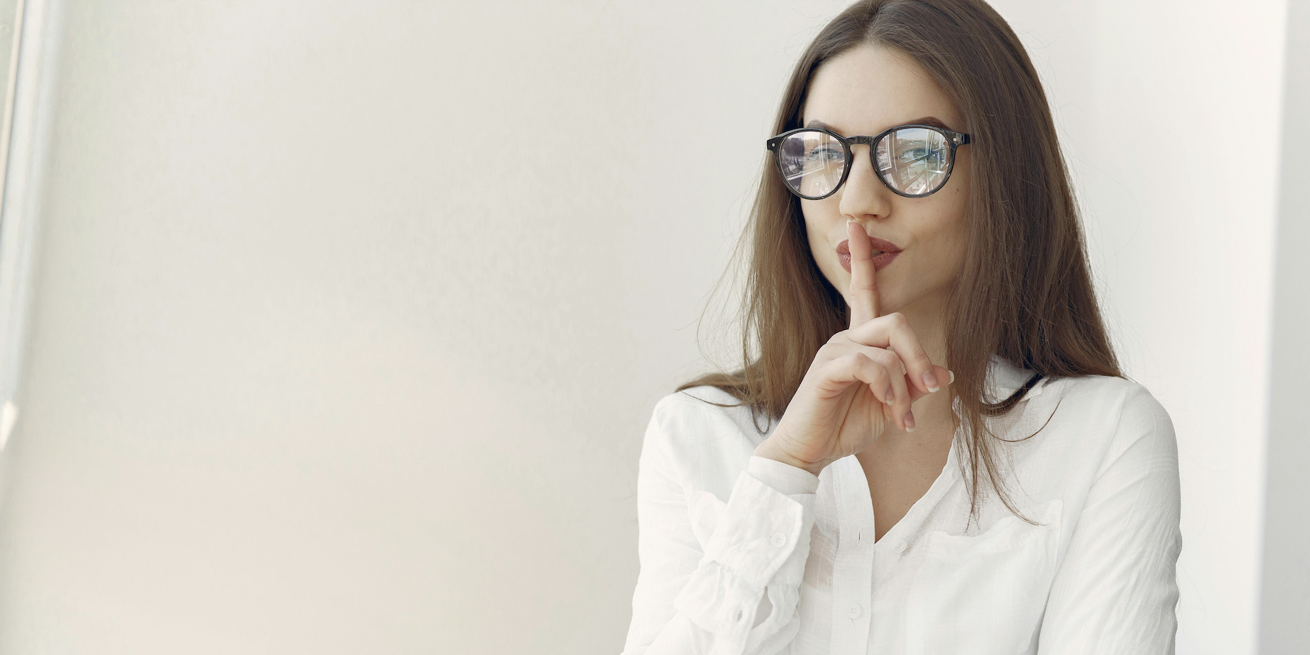 A woman sitting at a desk with her finger on her lips, indicating to be quiet.
