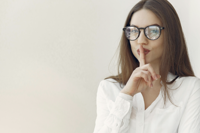 A woman sitting at a desk with her finger on her lips, indicating to be quiet.