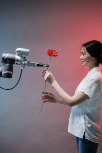 A robotic arm offers a flower to a smiling woman.