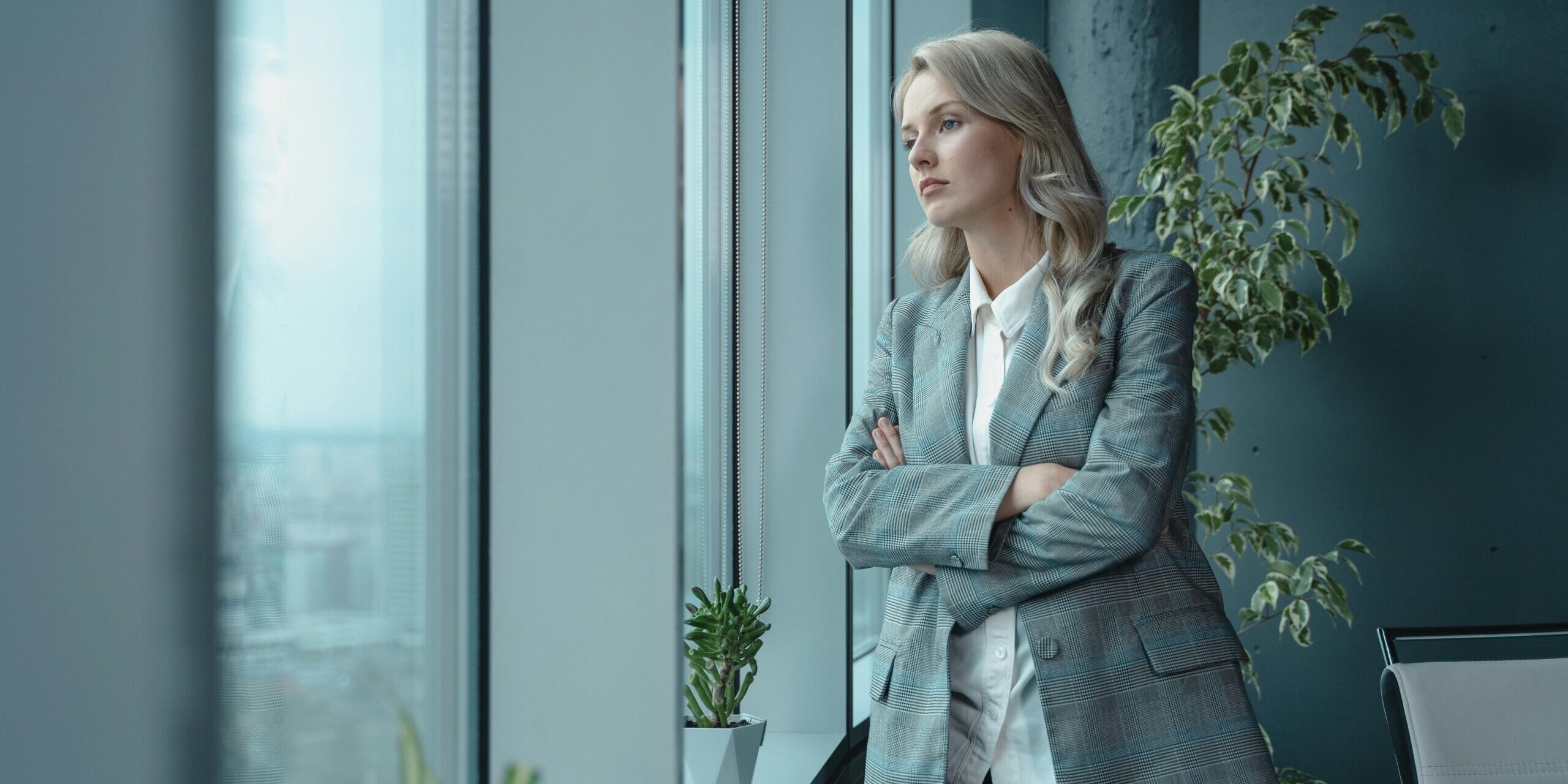 A businesswoman looking through a window in an office, appearing troubled.